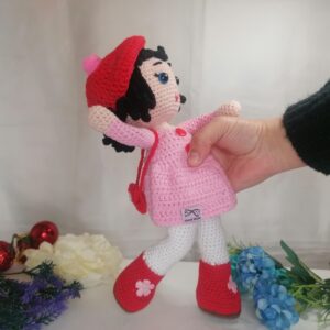Πλεκτή κούκλα με βαμβακερά νήματα, μήκους 31 εκ., ενδυμασία που περιλαμβάνει ένα ροζ πλεκτό φόρεμα, ένα καπέλο και παπούτσια σε έντονο κόκκινο χρώμα.