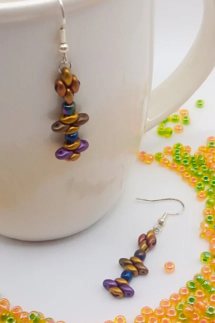 Tribal, κρεμαστά σκουλαρίκια μπάρες από Superduo χάντρες σε σατινέ υφή και σε ένα συνδυασμό γήινων τόνων του χρυσού, μπρονζέ, μωβ και καφέ. Κλείσιμο με γαντζάκι και στοπάκια σιλικόνης.