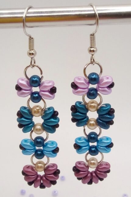 Μοντέρνα, κρεμαστά σκουλαρίκια μπάρες, φτιαγμένα από χάντρες Superduo σε σχέδιο λουλούδια και πεταλούδες. Σε έναν ενδιαφέροντα συνδυασμό πετρόλ, γαλάζιο, μωβ και ροζ με μαύρες λεπτομέρειες. 