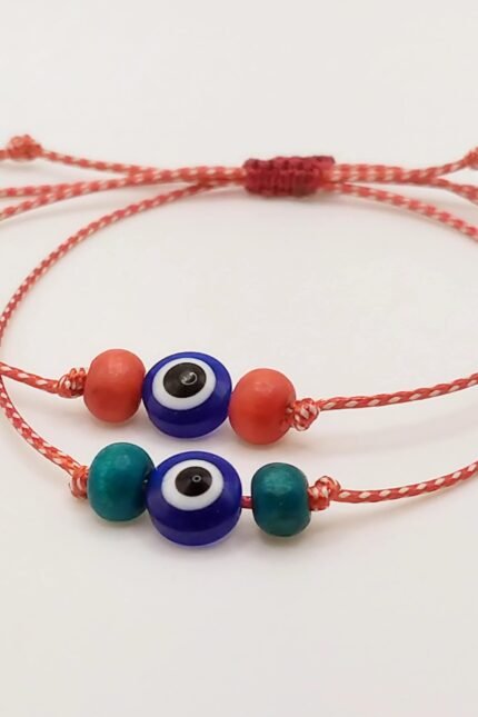 Μαρτάκι με ματόχαντρο (10mm) στο κέντρο, πλαισιωμένο από δύο ξύλινες χάντρες σε κόκκινο ή πετρόλ. Φτιαγμένο από μονό, γυαλιστερό μαρτιάτικο κορδόνι 2mm. Με αυξομειούμενο κλείσιμο ώστε να ταιριάζει σε κάθε καρπό. Σε δύο standard μεγέθη, ανδρικό και γυναικείο, αλλά μπορεί να γίνει και στο ακριβές μέγεθος που θέλετε.