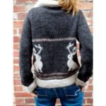 Πλεκτό πουλόβερ με φαρδιά γραμμή και εντυπωσιακό μοτίβο jackalope στην πλάτη, φορεμένο από γυναίκα μπροστά σε τούβλινο τοίχο.