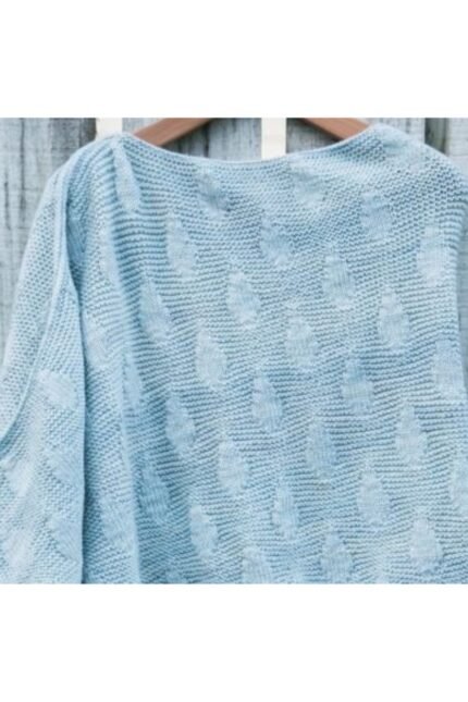 Πλεκτό πόντσο σε απαλό μπλε χρώμα με ασύμμετρο κόψιμο και ανάγλυφο σχέδιο σταγόνας, κρεμασμένο σε ξύλινη κρεμάστρα.