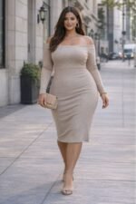 Plus-size brunette model wearing a beige off-the-shoulder ribbed midi dress, styled with gold hoop earrings, layered necklaces and a nude clutch, walking confidently on a modern city sidewalk. Based garment of our sewing pattern.