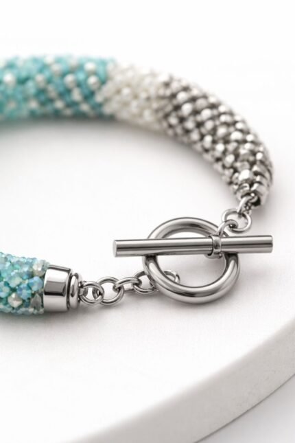 Stainless steel toggle clasp attached to a handmade beaded bracelet, close-up on white background.